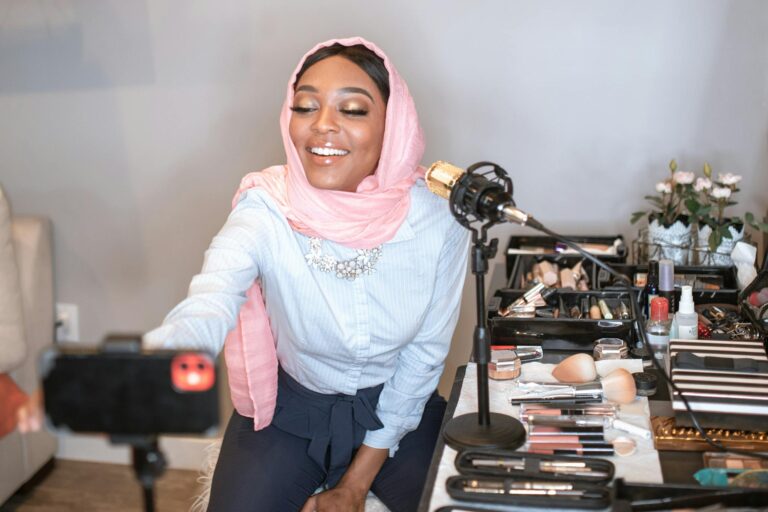 A beauty vlogger in a hijab recording a makeup tutorial with cosmetics setup.