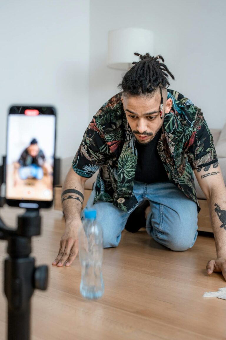 A man filming a bottle flip challenge on a smartphone indoors, capturing a trending social media moment.