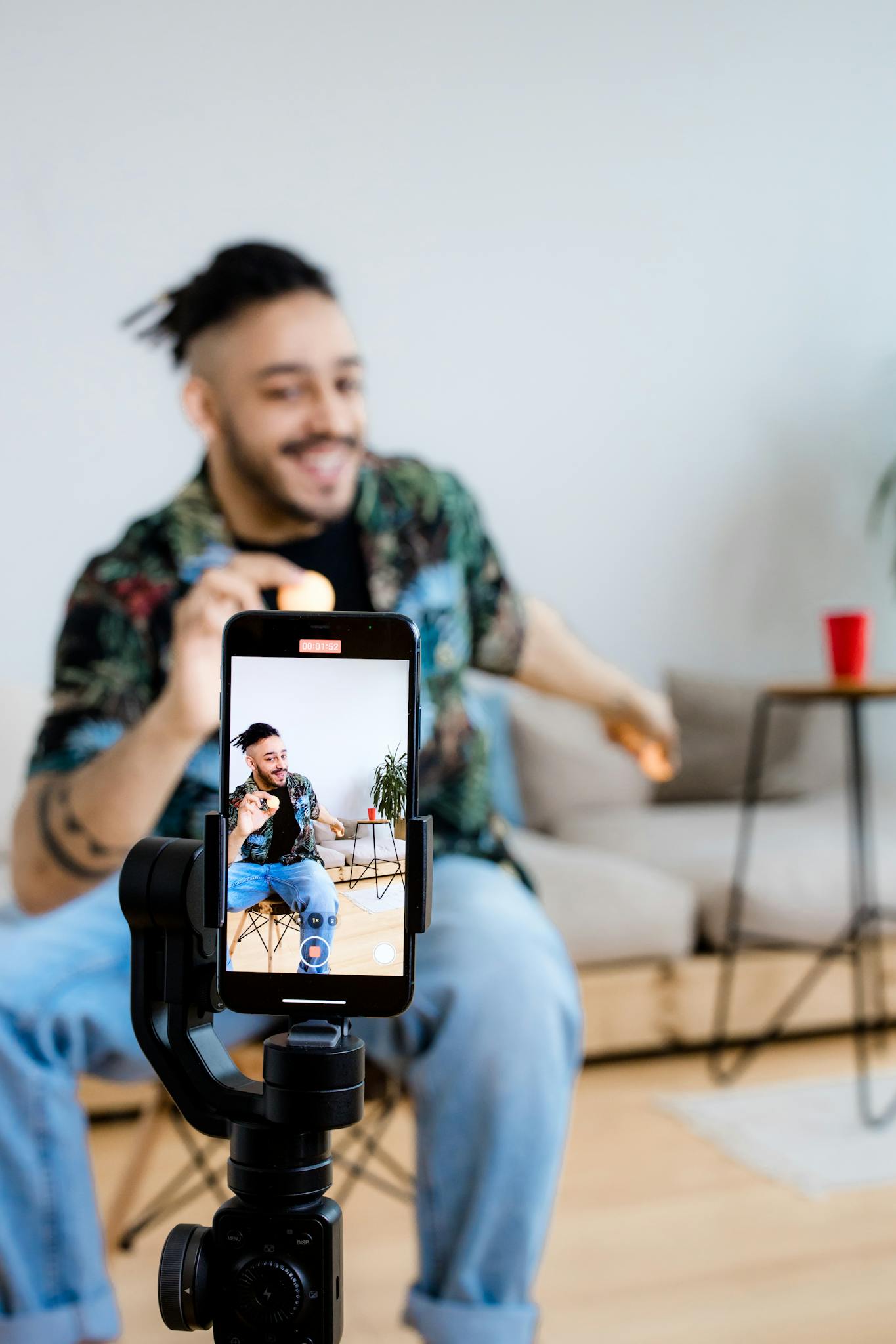 A young man vlogs indoors with a smartphone on a tripod, capturing engaging content.